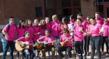 A group of Saint Lawrence students, wearing pink t-shirts, perform a musical number with instruments and a microphone, at the First-Year Cup Alma Mater Remix Competition.