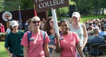 Two Saint Lawrence orientation leaders, holding a sign, lead a group of new Saint Lawrence students.