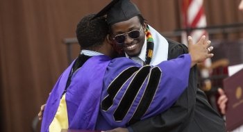 A graduate embraces a mentor at Commencement after receiving their diploma cover.