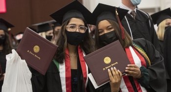 Two graduates hold up their diploma covers for the camera after Commencement.