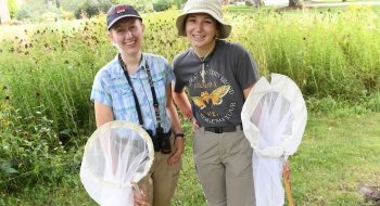 Two students stand in a field of wildflowers holding bug nets.