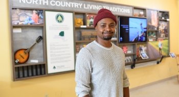Shedrack Bogonko '22 stands in front of a folk art display that reads &quot;North Country Living Traditions.&quot;