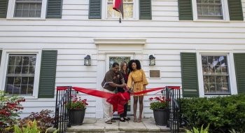 Hagi Bradley, President Kate Morris, and Diamond McAllister cut a big red ribbon on the front porch of a white two-story home with green shutters.