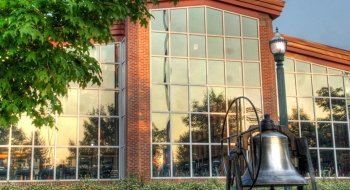A large silver bell stand is in the foreground with a large window-filled arena behind it.