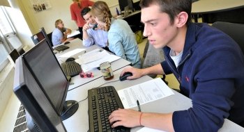 A Saint Lawrence University student uses a computer. A professor collaborates with a student in the background.