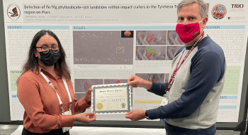 Anuva Anannya and Alexander Stewart hold a best poster award together at the Geological Society's annual conference. Anuva's award-winning poster on Mars is in the background.