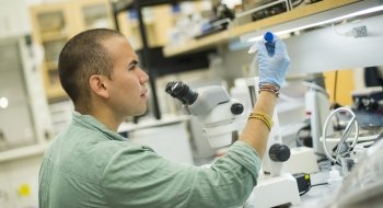 A Saint Lawrence University student, wearing a lab coat, examines a vial in a research lab.