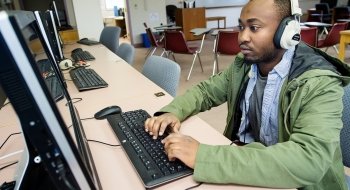 A student, wearing headphones and a green jacket, uses a computer at Saint Lawrence University.