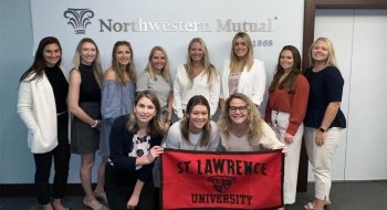 A group of 11 Laurentians stand in front of a Northwestern Mutual sign while holding a Saint Lawrence University banner.