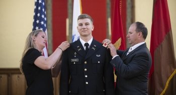 A photo of Garnet Williams having pins and parts of his uniform put on as he stands between flags.