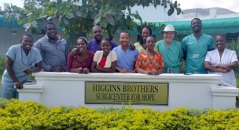 A photo of Ted Higgins and peers smiling around the sign to the Higgins Brothers Surgicenter for Hope