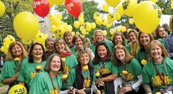 A photo of Kappa Delta Sigma alum all wearing the same shirts posing as dozens of balloons float above them.
