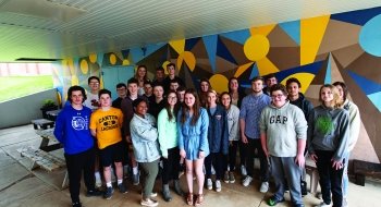 A photo of St Lawrence and Canton Central School students outside of a vibrantly colored mural.