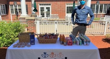 St Lawrence alumni Conor McDermott standing at a table full of snacks and drinks outside the brick wall entrance of Kind Senior Care, a nonmedical home care business.