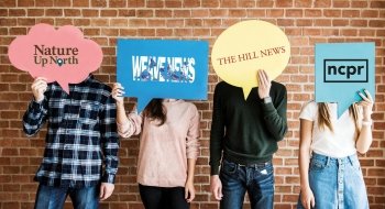 A photo of students holding up signs in front of their face, each with a different journalism group on campus' logo printed on it. One for Nature up North, one for Weave News, one for The Hill News, and one for NCPR.