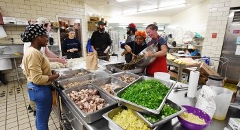 A photo of students in a large kitchen preparing a meal together.