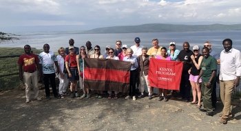 A photo of St Lawrence students and partners in Kenya standing in front of a picturesque lake holding St Lawrence flags.