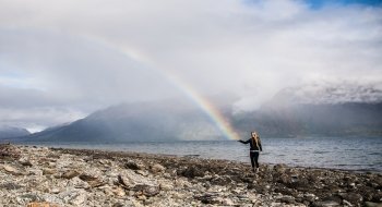 A photo of St Lawrence student on the beach with a half of the rainbow in the sky looking like the end is on the student's palm.