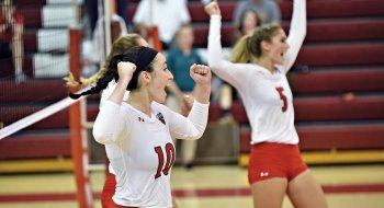A photo of volleyball player Grace Kelly cheering with her arms raised while on the court.