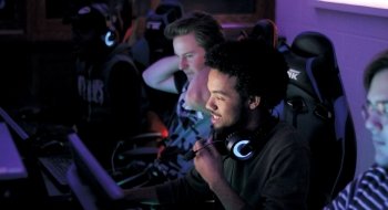 A photo of a line of students in large gaming chairs sitting at computers smiling.