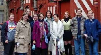A group of students in warm clothing stand in front of a red and white building in Rennes, France.