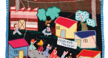 A photo of an arpillera that features brightly colored houses and people.