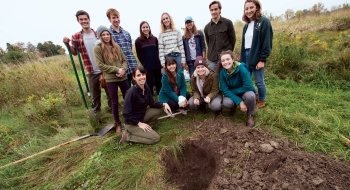 A photo of Ceramics 1 students posing in a field behind a large hole they dug.