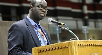 A photo of Okoth standing behind a podium.