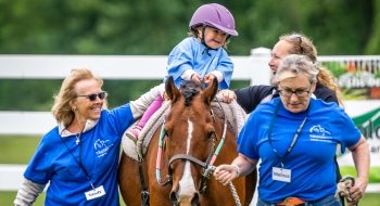 Members of Equicenter helping a smiling child ride a horse.