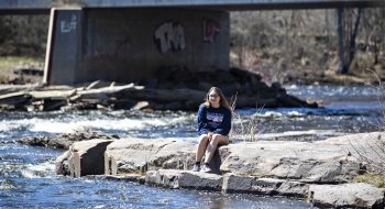 A woman sitting on rocks in the middle of a calm river
