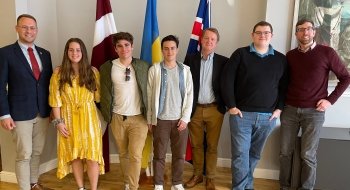 Saint Lawrence students, studying abroad in London, stand in front of the flags of Latvia, Ukraine, and the United Kingdom at the Embassy of Latvia in London, England.