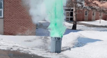 Green mist pours out of a grey garbage can sitting in the snow on a sunny day.