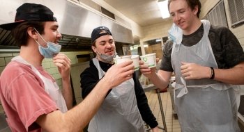 Three students cheers their cups of hot chocolate in a ktichen.