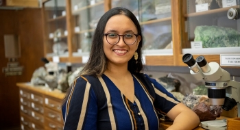 Anuva Anannya stands next to a microscope in a geology lab.