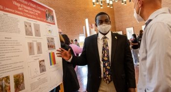 A student stands next to a large research poster and explains their project to a Festival Day attendee.