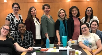 A group of Saint Lawrence faculty members stand near a long table while attending a professional development retreat.
