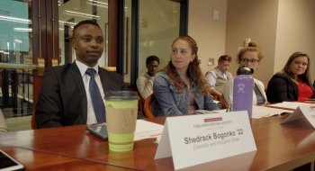 Shedrack Bogonko '22 sits at a glossy conference table, wearing a suit and tie, during a student government meeting.