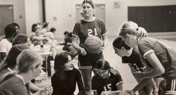 A black and white photo of Saints Women's Basketball huddled up on the sidelines of the court.