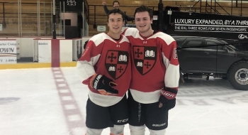 Tommy Benjes puts his arm around a teammate. They're standing on an ice rink and wearing Saint Lawrence hockey uniforms.