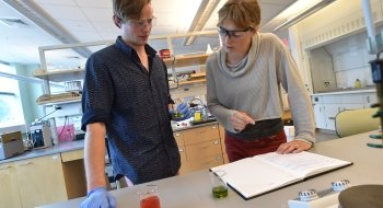 Sam Glazer, professor of chemistry, works along side a Saint Lawrence student in the research lab. They are wearing protective goggles.