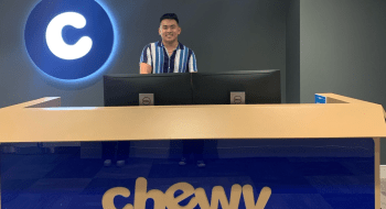 Andrew Han stands behind a large desk with the blue &quot;Chewy&quot; logo on it.