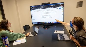 Sam Cohen and Anne Marie Hubert look at a word document displayed on a large television screen.