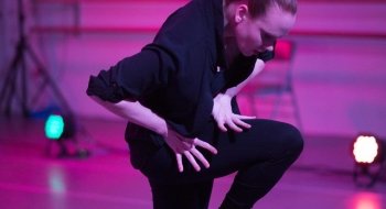A woman in black dances in a studio filled with pink light