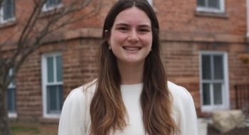 Headshot of Elena Lindquist, wearing a white sweater and standing in front of a brick building.