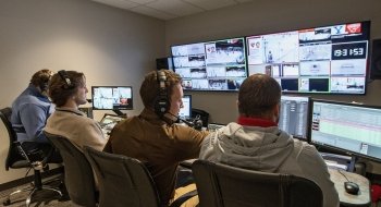 Four men sit in a row of chairs at a desk in the Appleton Media Booth while managing in-arena entertainment for the night's hockey game.