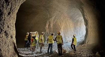 A group of students, wearing neon construction vests and hard hats, examine a cave.