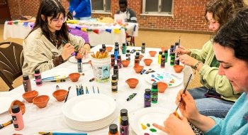 A group of Saint Lawrence students sit at a table and paint in celebration of international education week.