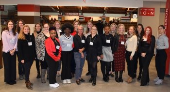 Several Laurentians, wearing business casual attire, stand together and smile at Appleton Arena as part of the Saint to Saint Women's Summit.