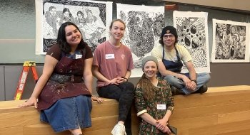 Four people wearing name tags sit and stand in front of black and white posters of print artwork.
