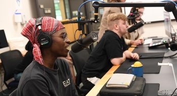 A student wearing a checkered headscarf speaks into a microphone in the University's podcasting studio.